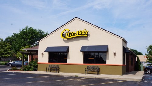 Exterior of a restaurant named "Chicago's," featuring a light-colored building, large windows, and outdoor seating.