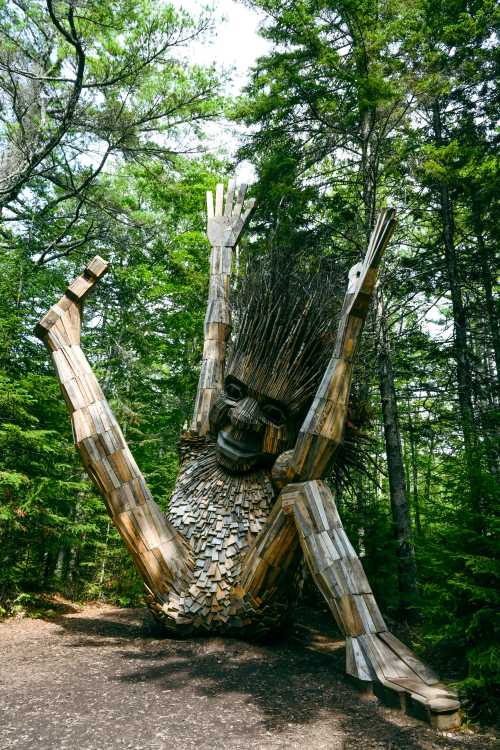 A large wooden sculpture of a figure with raised arms, surrounded by lush green trees in a forest setting.