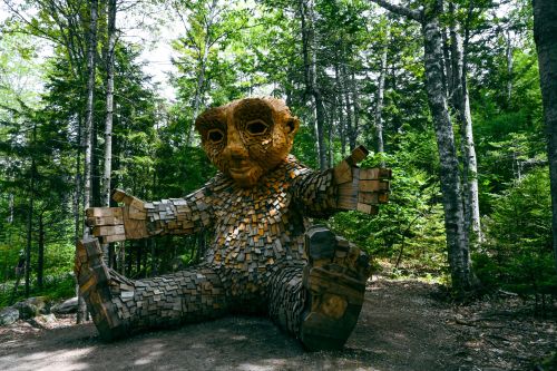 A large wooden sculpture of a seated troll-like figure surrounded by trees in a forest setting.