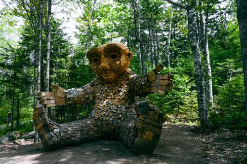 A large wooden sculpture of a seated troll-like figure surrounded by trees in a forest setting.