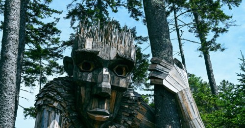 A large wooden sculpture of a giant figure among tall trees, with intricate details and a striking expression.
