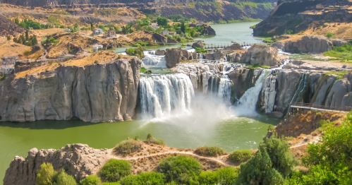 A scenic view of a waterfall cascading into a green river, surrounded by rocky cliffs and lush vegetation.