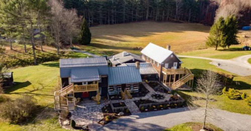 Aerial view of a large rustic house with a stone pathway, surrounded by trees and an open field.