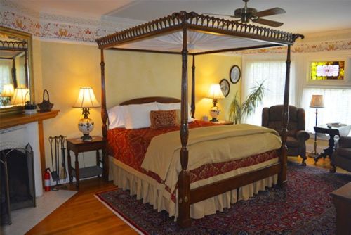 Cozy bedroom featuring a four-poster bed, warm lighting, and elegant decor with a plush rug and comfortable seating.