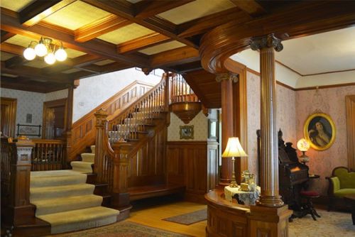 Elegant foyer with a grand staircase, wooden paneling, vintage decor, and a warm, inviting atmosphere.