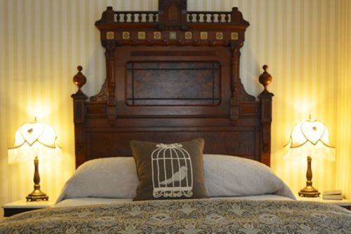 A cozy bedroom featuring a wooden headboard, decorative lamps, and a pillow with a birdcage design.