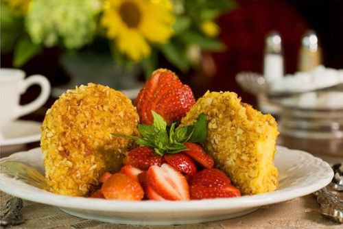 A plate of golden, crispy fried balls served with fresh strawberries and a sprig of mint, set on a decorative table.