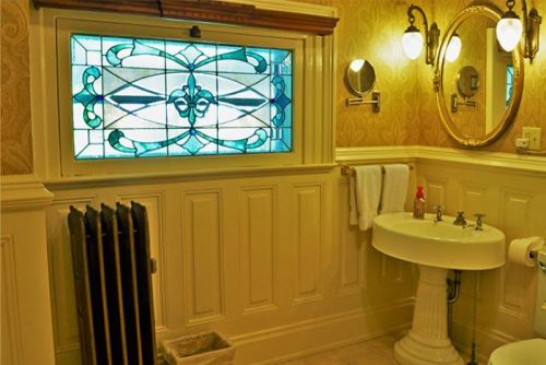 A vintage bathroom featuring a stained glass window, pedestal sink, and decorative wall paneling.