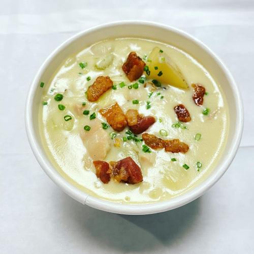 A bowl of creamy soup with potatoes, bacon bits, and chives, served in a white cup.