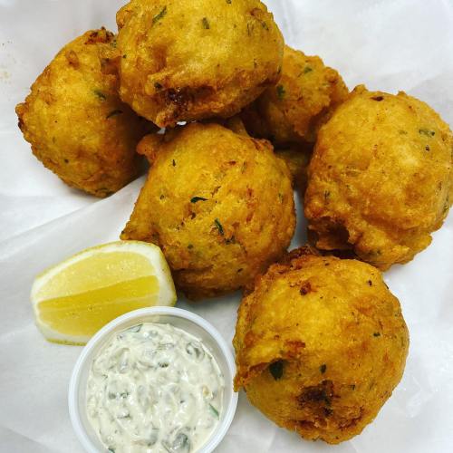 A plate of golden-brown fritters with herbs, served with a lemon wedge and a small cup of dipping sauce.