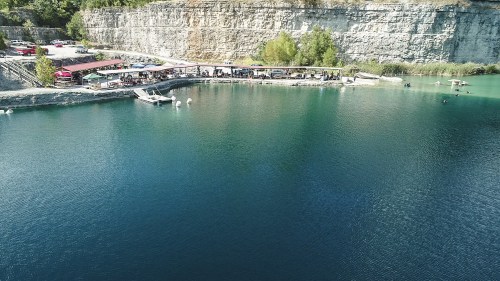 Aerial view of a clear blue lake surrounded by rocky cliffs, with people enjoying activities along the shore.
