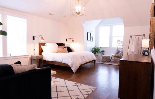 Bright, modern bedroom with a large bed, stylish decor, and natural light from windows. Cozy seating area included.