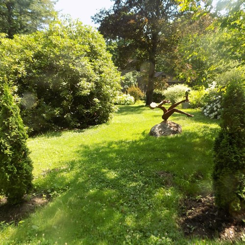 A lush garden with green grass, shrubs, and a sculpture on a rock surrounded by trees and flowers.