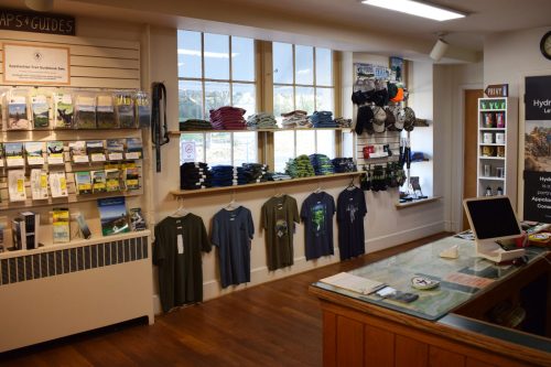 A retail space featuring outdoor gear, maps, and clothing displayed on shelves and walls, with a counter in the foreground.