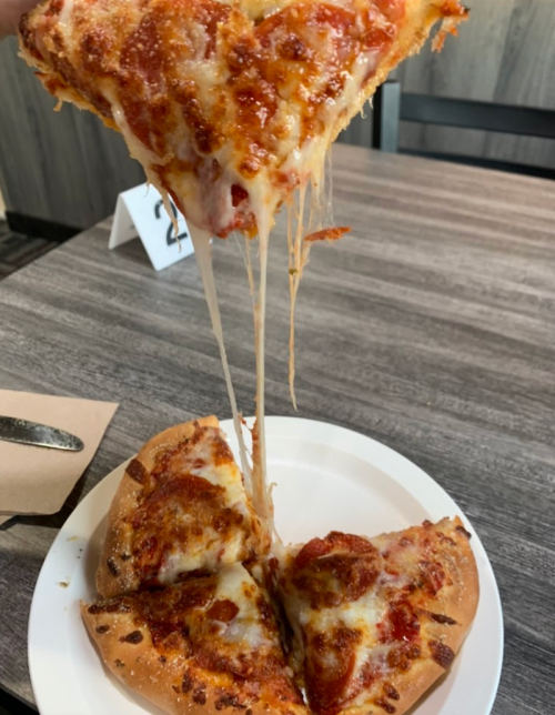 A slice of cheesy pepperoni pizza being lifted, with gooey cheese stretching from the pie on a white plate.