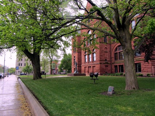 A red brick building with large windows, surrounded by green trees and grass, on a rainy day.
