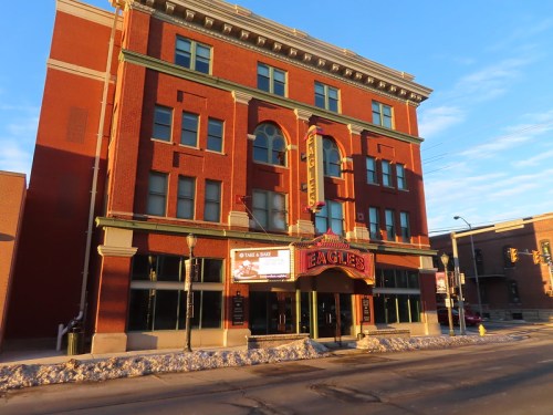 Historic red brick building with "Eagles" sign, featuring large windows and a marquee, under a clear blue sky.