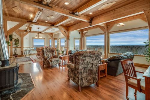 Spacious living area with wooden beams, large windows, and cozy seating, overlooking a scenic landscape.