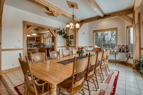 A spacious dining room with a large wooden table, surrounded by chairs, and large windows letting in natural light.