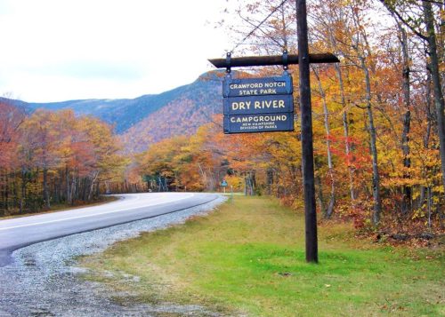 Sign for Dry River Campground at Crawford Notch State Park, surrounded by autumn foliage and a winding road.