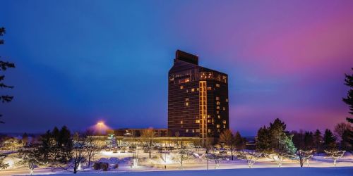 A tall hotel building illuminated at dusk, surrounded by snow-covered trees and a colorful sky.