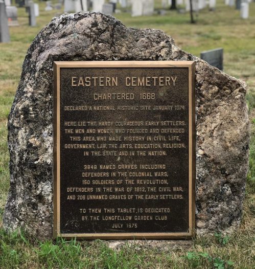 A stone tablet at Eastern Cemetery, detailing its history and significance, surrounded by trees and grass.