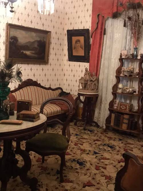 A vintage room with patterned wallpaper, a plush sofa, ornate furniture, and decorative items on shelves.