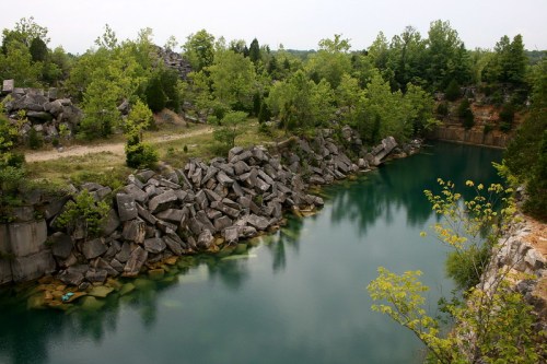 A serene quarry with clear blue water, surrounded by lush greenery and rocky cliffs.