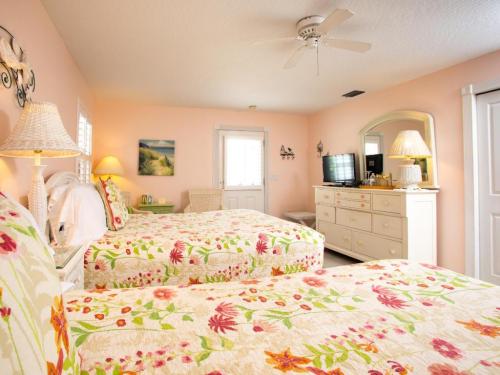 Brightly decorated bedroom with two floral-patterned beds, a dresser, and a door leading outside. Soft pastel colors.