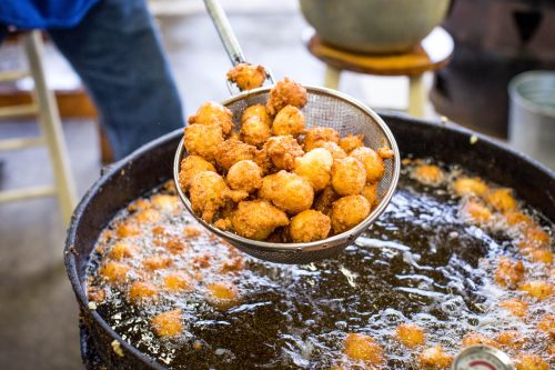 A metal strainer lifts golden-brown fried food from a bubbling pot of oil.