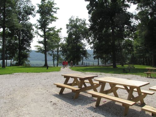 A scenic park with picnic tables, trees, and a path leading to a distant view of hills and people walking.
