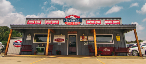 A rustic storefront with a sign reading "Townsend Cafe & Supply," featuring various advertisements and a blue sky.