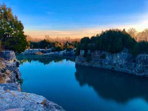 A serene landscape featuring a calm blue lake surrounded by rocky cliffs and lush greenery under a clear sky.