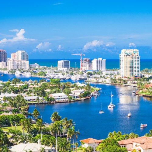 A scenic view of a coastal city with skyscrapers, boats, and lush greenery under a clear blue sky.