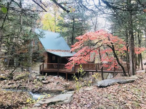 A cozy cabin surrounded by trees and colorful autumn foliage, with a small stream nearby.