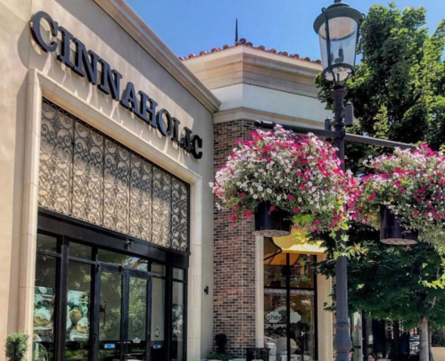 Exterior of Cinnaholic bakery with decorative hanging flower baskets and a clear blue sky.