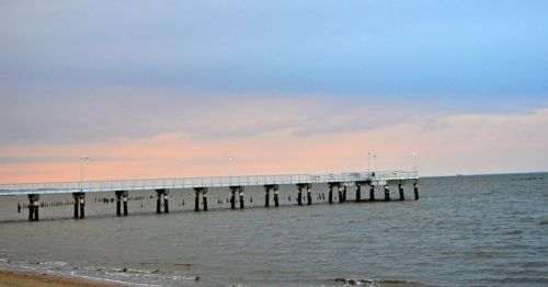 A wooden pier extends into calm waters under a pastel sky at dusk.