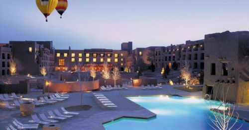 A serene resort scene at dusk, featuring a pool, lounge chairs, and hot air balloons in the sky.