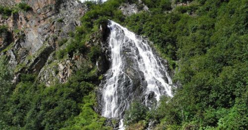 A cascading waterfall surrounded by lush green foliage and rocky cliffs.