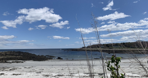 A serene beach scene with rocky shorelines, calm water, and a clear blue sky dotted with clouds.