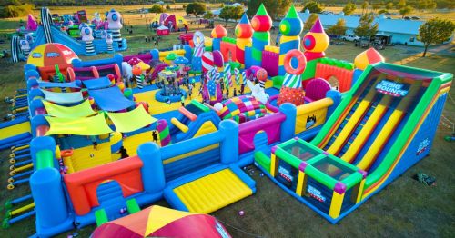 A colorful inflatable bounce park with slides, castles, and various play areas, filled with people enjoying the attractions.