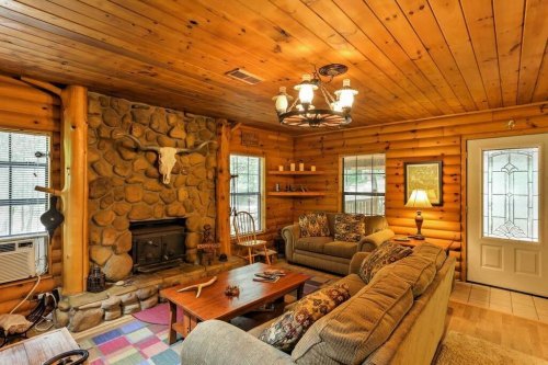 Cozy log cabin living room with stone fireplace, wooden walls, comfortable sofas, and a welcoming front door.