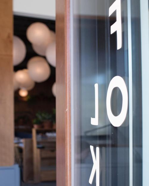 Close-up of a glass door with the word "FOLK" partially visible, with soft, round lights in the background.