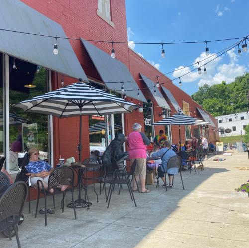 A lively outdoor café scene with patrons sitting under striped umbrellas, enjoying the sunny day along a brick building.