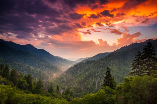 A vibrant sunset over a lush green valley, framed by mountains and dramatic clouds.