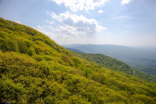 Lush green hills under a bright sky with scattered clouds, showcasing a serene mountain landscape.