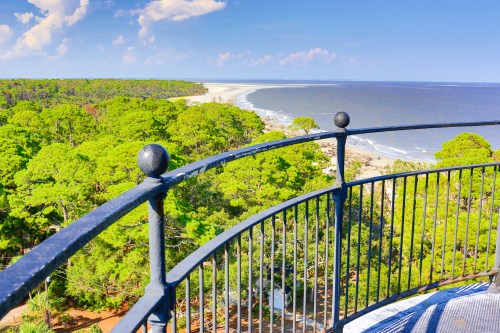 A scenic view from a lighthouse balcony overlooking a coastline with lush greenery and calm waters.