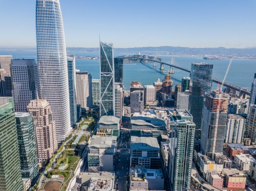 Aerial view of a modern city skyline with skyscrapers and a bridge over water in the background. Clear blue sky.
