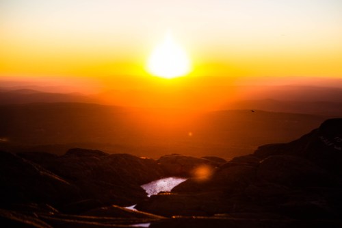 A vibrant sunset over a mountainous landscape, with warm orange and yellow hues illuminating the sky.