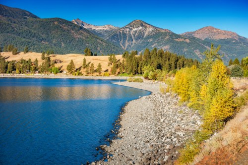 Scenic view of a calm lake surrounded by mountains and colorful autumn trees under a clear blue sky.